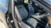 Interior of a black leather car showing two front seats, center console, and open door with sunlight on the seats.