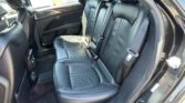 Back seat of a car with black leather upholstery, three seats and visible seat belts in a sunlit interior window view outside the door panel.