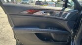 Close-up of a car front door interior showing a wood trim strip, chrome door handle, and window/lock controls; outside lot with vehicles.