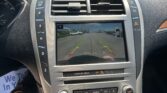 Center console car display showing rearview camera view with guiding green, yellow, and red lines over a parking lot behind the vehicle.