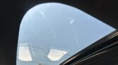 View through a car's open sunroof showing a clear blue sky and reflections on the glass edge of the pane.