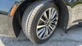 Close-up of a black car wheel with alloy rim and treaded tire, reflections visible on the body panel behind it.