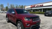 Red SUV (Jeep Grand Cherokee) parked in front of EZ LOAN Auto Sales dealership on a sunny day.