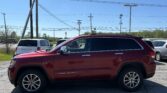 Red Jeep Grand Cherokee parked in a lot with power lines and poles overhead against a clear blue sky.