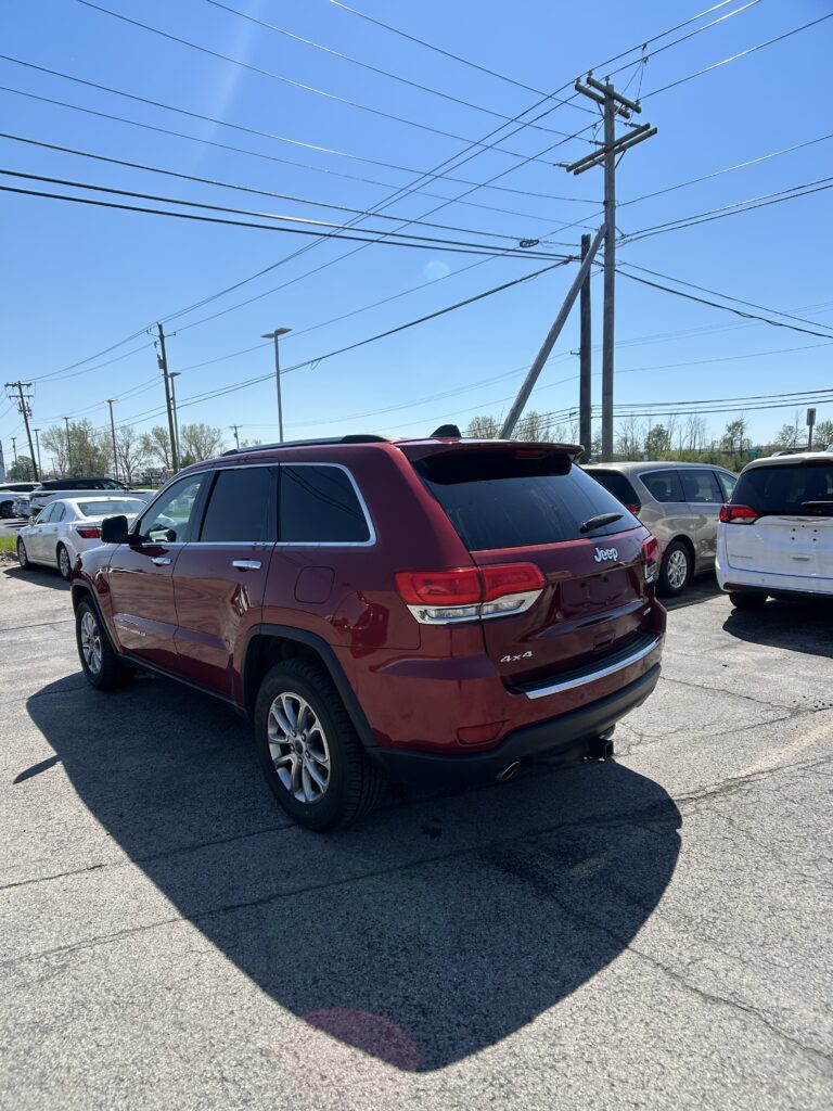 Red SUV parked in a lot under power lines against a clear blue sky while other cars are nearby.