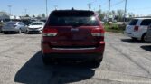 Rear view of a red Jeep SUV in a parking lot with other cars and power lines overhead on a sunny day