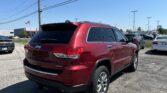 Red Jeep SUV parked diagonally in a bright dealership lot with power lines overhead and other cars in the background