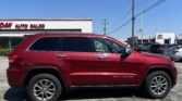 Red SUV parked in a dealership lot with a white building that reads 'Auto Sales' in the background under a clear blue sky