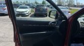 Open car door from inside, view of a crowded parking lot with multiple cars and a clear blue sky beyond the windshield side window.
