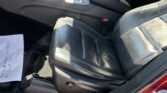 Front seating area of a red car with black leather seats, center console with gear shifter and armrest, and a paper on the floor.
