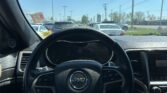 View from the driver’s seat of a Jeep: steering wheel and dashboard, looking out at a busy parking lot under a clear blue sky.