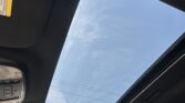 Interior of a car ceiling with a large panoramic sunroof and blue sky visible