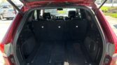 Rear of a red SUV with the hatch open, exposing a large cargo area and folded rear seats, plus a trailer hitch nearby.