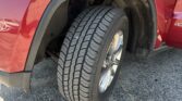 Front right wheel and fender of a red SUV, showing the tire tread and black wheel well trim in a parking lot.
