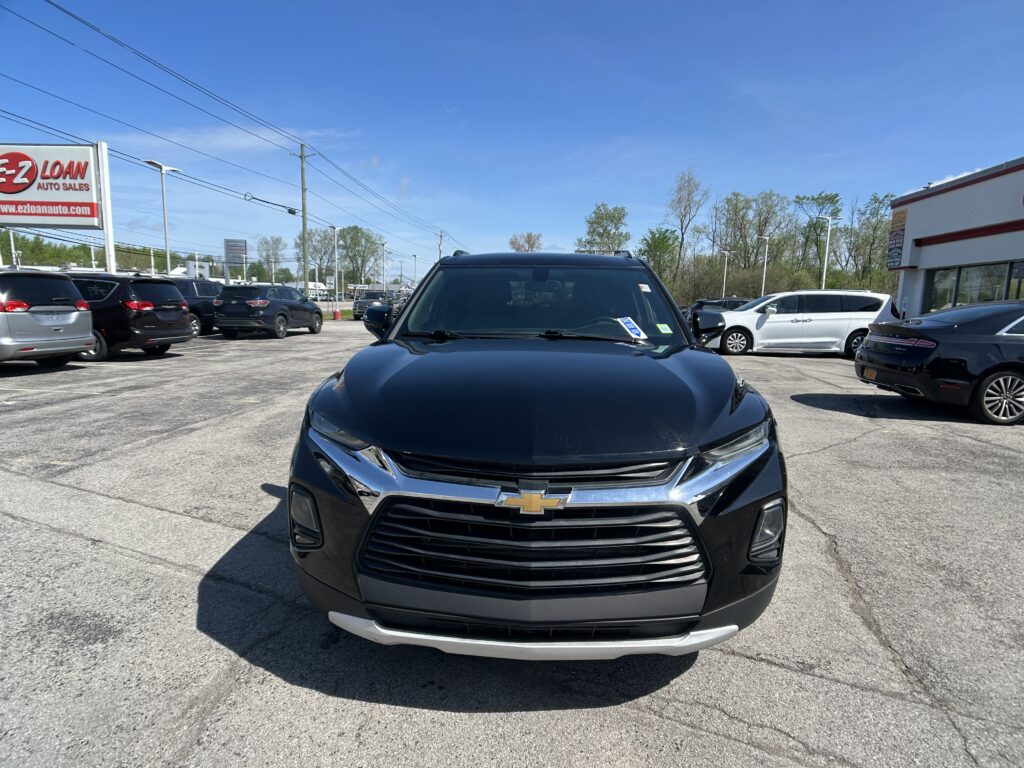 Front view of a black Chevrolet SUV in a busy car dealership lot, with other cars and a red EZ Loan sign in the background.