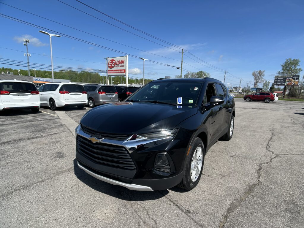 Close-up of a black SUV in the dealership lot with white vans behind and an EZ LOAN Auto Sales sign in the background.