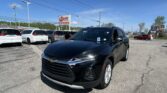 Close-up of a black SUV in the dealership lot with white vans behind and an EZ LOAN Auto Sales sign in the background.