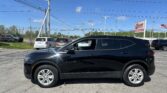 Close-up of a shiny black SUV in a dealership lot with other cars and a blue sky above.