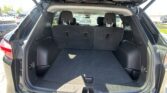 Open SUV cargo area with third-row seats upright and black carpeting visible in the trunk.,