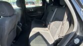Back seat area of a car with three seat belts and dark fabric upholstery, visible outside parking lot through the window.