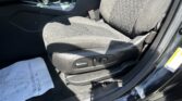 Front left area of a car interior showing the driver's seat, center console, seatbelt buckle, and a sheet of paper on the floor beneath the seat.