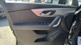 Close-up of a car interior door panel with silver door handle and window/lock controls; outside dealership lot visible through window.