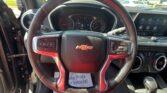 View of the driver’s seat interior with steering wheel, gauges, and a touchscreen—parking lot visible through the windshield.