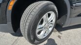 Close-up of a car tire and silver alloy wheel with visible tread, fender, and orange side marker on a dark vehicle