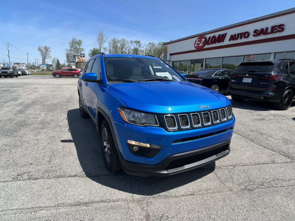 Blue Jeep SUV parked in a dealership lot with EZ Loan Auto Sales building in the background and other vehicles around.