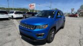 Blue Jeep SUV in the foreground at a car dealership lot with white minivans behind and an EZ Loan sign in the background.