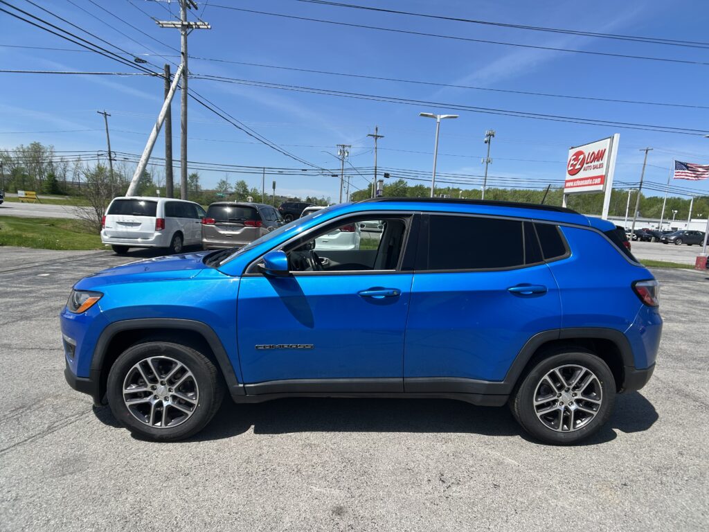 Blue SUV (Jeep Compass) in a dealership lot with other cars and an EZ Auto Loans sign in the background.