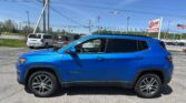 Blue SUV (Jeep Compass) in a dealership lot with other cars and an EZ Auto Loans sign in the background.