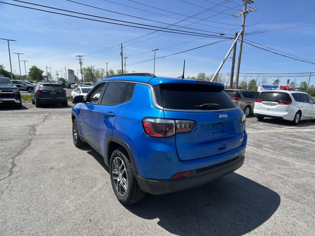 Blue Jeep SUV in a dealership lot with other cars and power lines overhead on a sunny day.