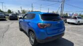 Blue Jeep SUV in a dealership lot with other cars and power lines overhead on a sunny day.