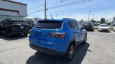 Blue Jeep SUV foreground in a car dealership lot with other vehicles and a Toyota sign on a building in the background, under a blue sky.