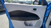 Interior of a blue car door with light gray panel, chrome door handle, and window controls; parking lot outside viewed through the window.