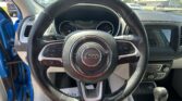 Close-up view of a Jeep steering wheel from the driver's seat, with the blue car door open and the dashboard in the background