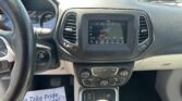 Interior view of a car cabin showing the steering wheel, center touchscreen, and gear shifter, with a flyer on the passenger side floor that reads “We Take Pride in Your Vehicle.”