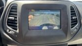 Car dashboard with rear-view camera display showing a parking lot and guiding lines; on-screen text reads 'Check entire surroundings'