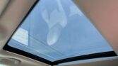 Interior of a car showing a panoramic sunroof with the blue daytime sky visible through it, beige headliner surrounding the opening.