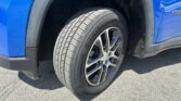 Close-up of a blue vehicle's front wheel and tire, showing the tread and alloy rim inside a black wheel well trim