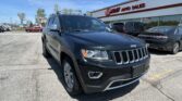 Front-left view of a dark Jeep SUV in the dealership lot in front of EZ Auto Sales building with other cars nearby.