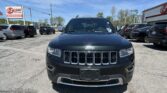 Front view of a dark Jeep SUV at a car dealership, with other cars and an E-Z Loan sign in the background under a blue sky.