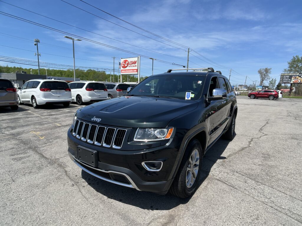 Black Jeep SUV in foreground at a car lot with white vans and a red E-Z Loan sign in the background under a blue sky