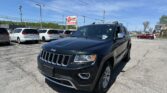 Black Jeep SUV in foreground at a car lot with white vans and a red E-Z Loan sign in the background under a blue sky