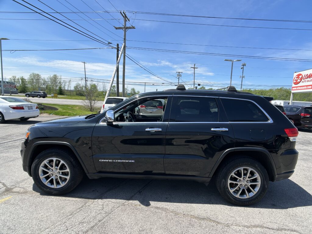 Close-up of a black Jeep Grand Cherokee parked in a lot, with power lines and a blue sky above.