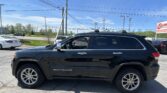 Close-up of a black Jeep Grand Cherokee parked in a lot, with power lines and a blue sky above.