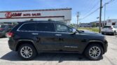 Black Jeep Grand Cherokee SUV in a dealership lot with an E-Z Loan Auto Sales building in the background.