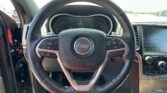 Steering wheel with Jeep logo centered, car dashboard and infotainment screen visible inside a vehicle.