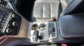 Front interior of a car showing a leather driver seat, center console with climate controls, and cup holders with keys resting inside.